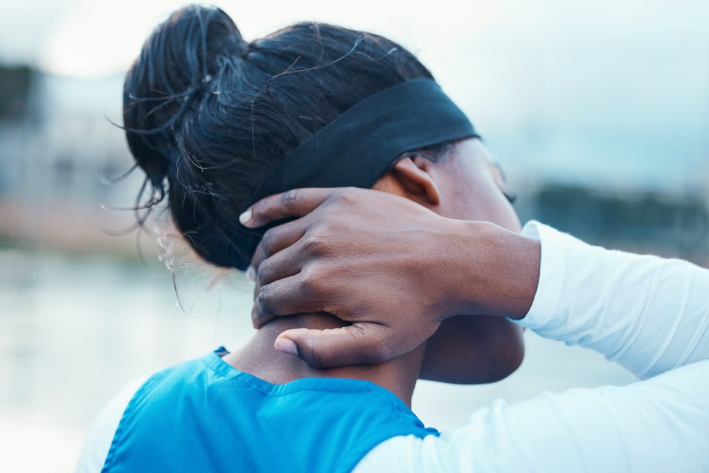 Sample Post: A person wearing a headband and blue top is holding the back of their neck with one hand, viewed from behind.