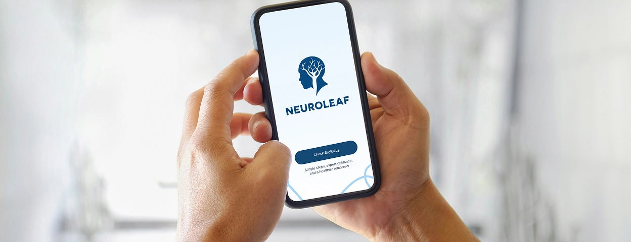 A person holds a smartphone displaying the Neuroleaf app login screen, featuring a brain logo inside a head outline and two login buttons.